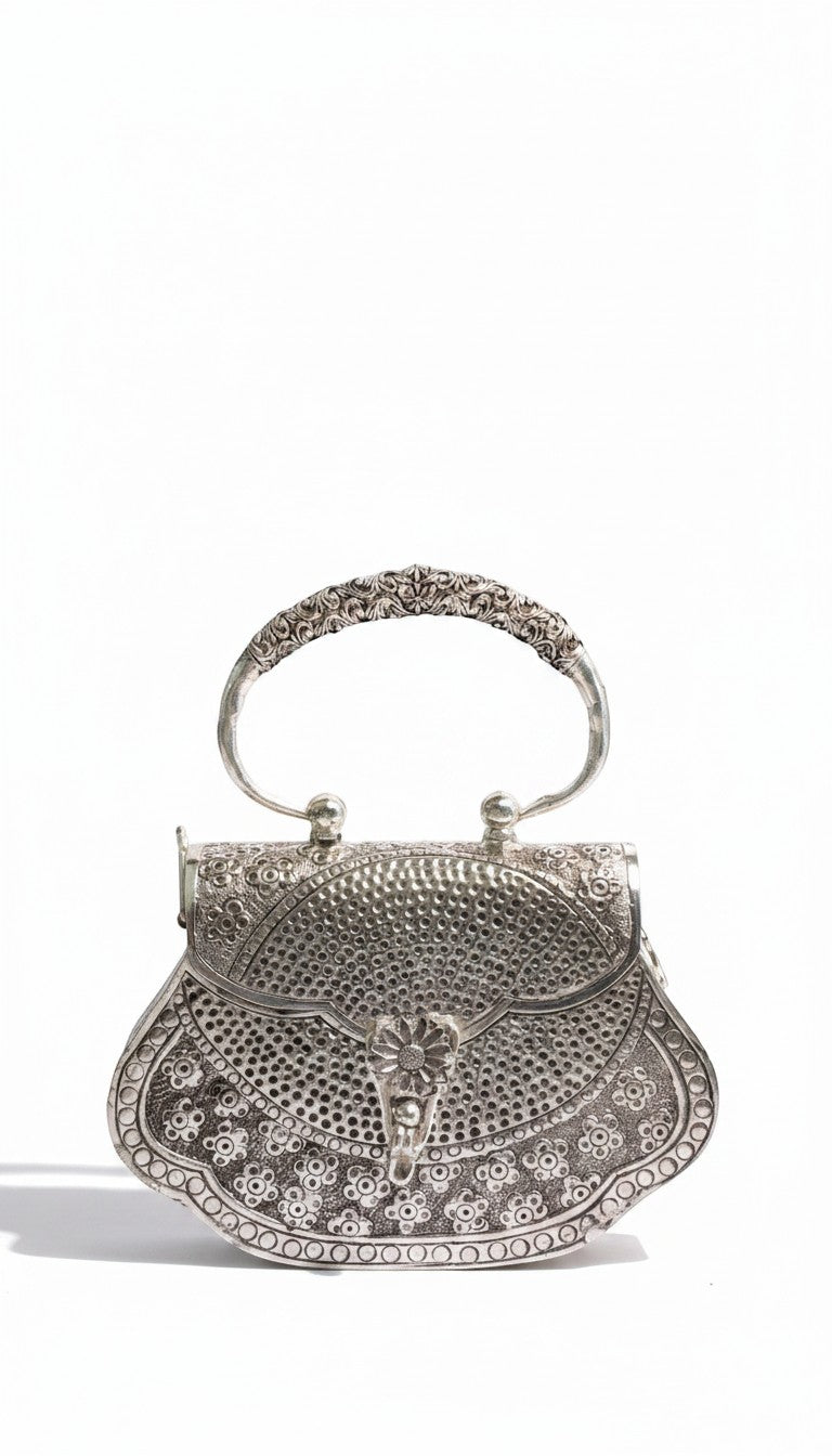 Rigvedaa™ Kanak Silver Clutch, a silver-plated brass purse with intricate hand-carved detailing and a floral clasp. Features a decorative handle and ornate filigree.