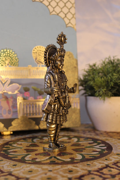Side view of brass Narayan Swami temple idol with ornate sun disc backdrop showing profile details and mukut crown