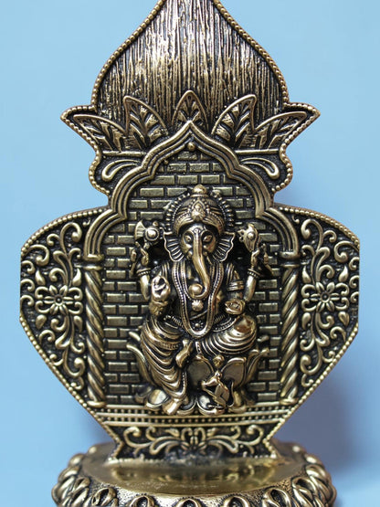 Rigvedaa™ antique gold Ganesha idol in an ornate arch frame with intricate floral motifs and lotus pedestal detail.