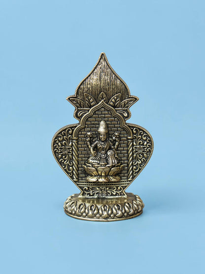 Rigvedaa™ antique gold Lakshmi idol in an ornate arch frame with floral motifs and a lotus pedestal on a blue background