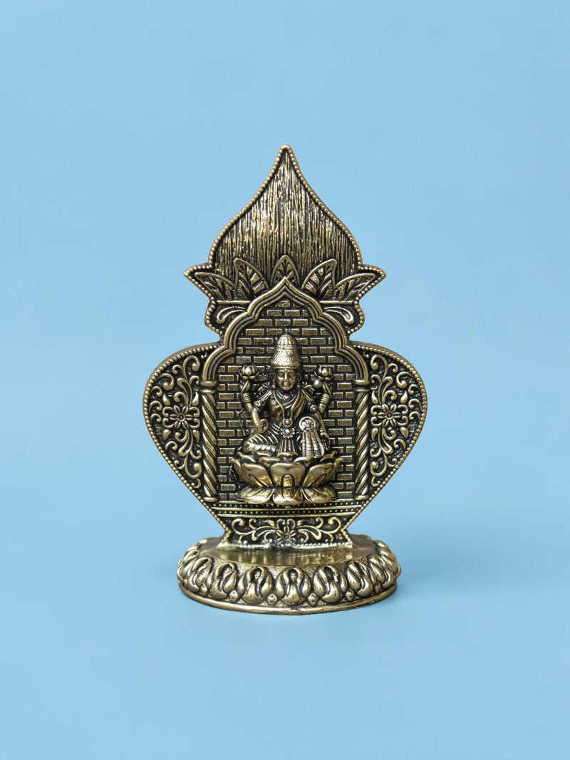 Rigvedaa™ antique gold Lakshmi idol in an ornate arch frame with floral motifs and a lotus pedestal on a blue background