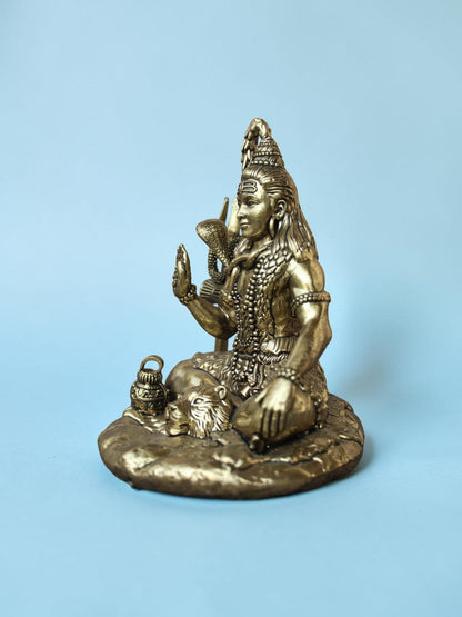 Rigvedaa™ antique gold Lord Shiva idol in a meditative seated pose with a trishul and serpent on a light blue background