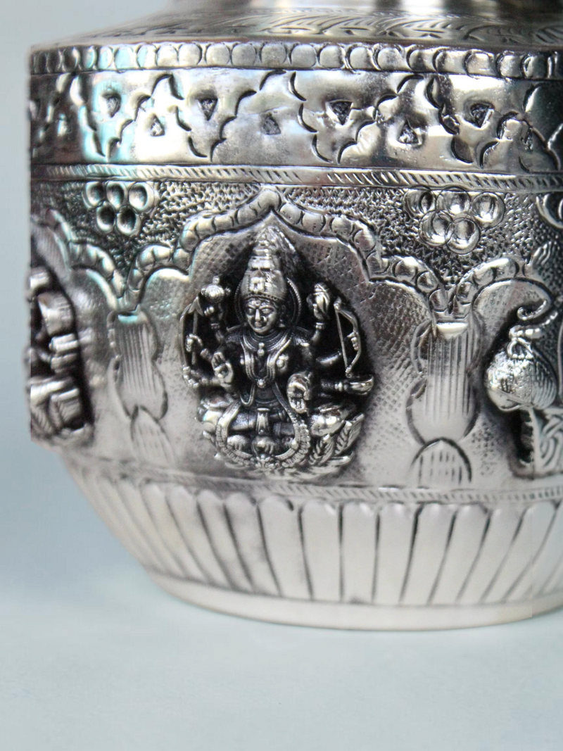 Rigvedaa™ silver plated brass Ashta Lakshmi kalash featuring intricate embossed goddess figures and floral motifs.