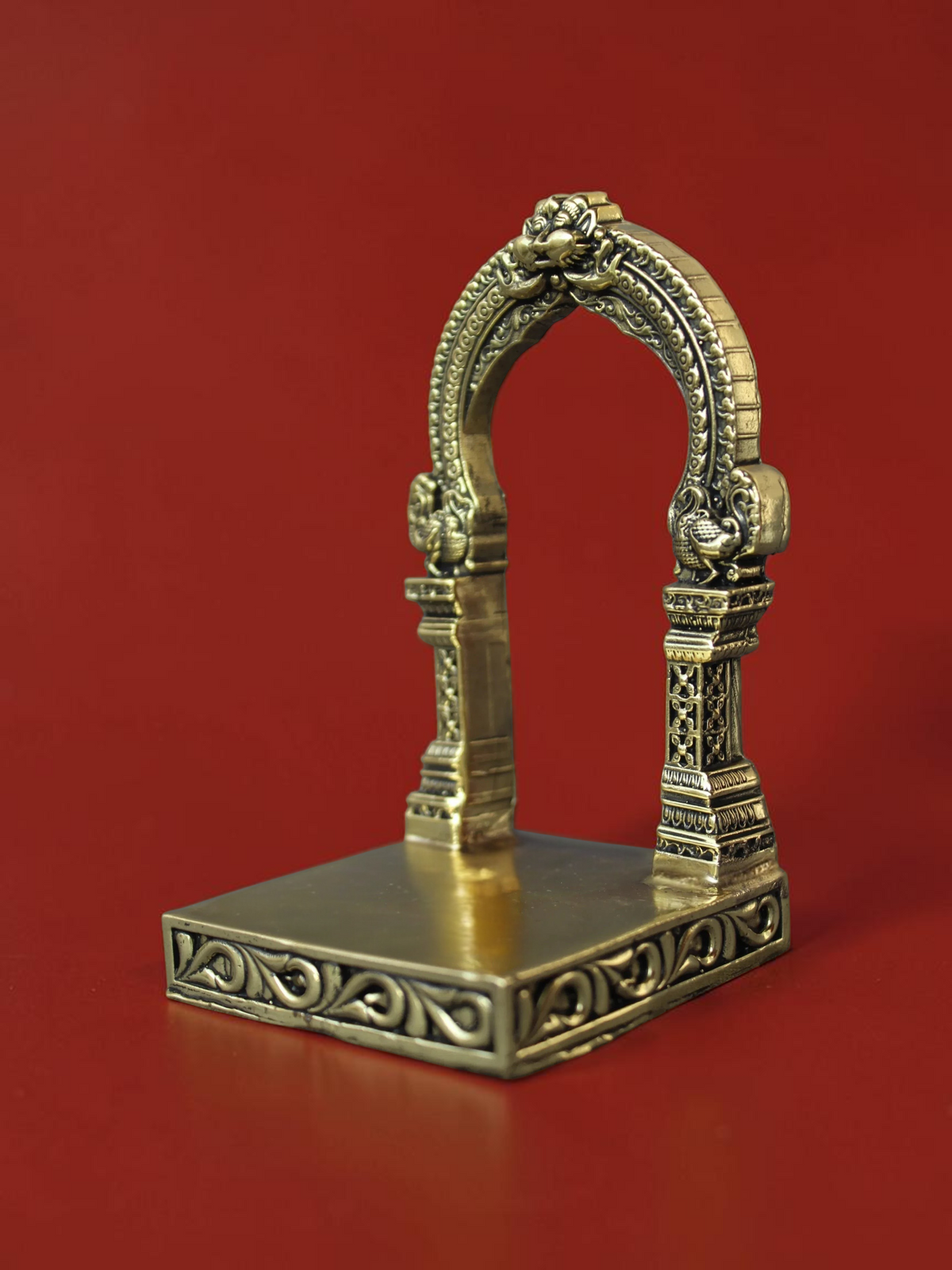 Rigvedaa™ handcrafted brass archway idol stand with intricate carvings and ornate scrollwork on a square base