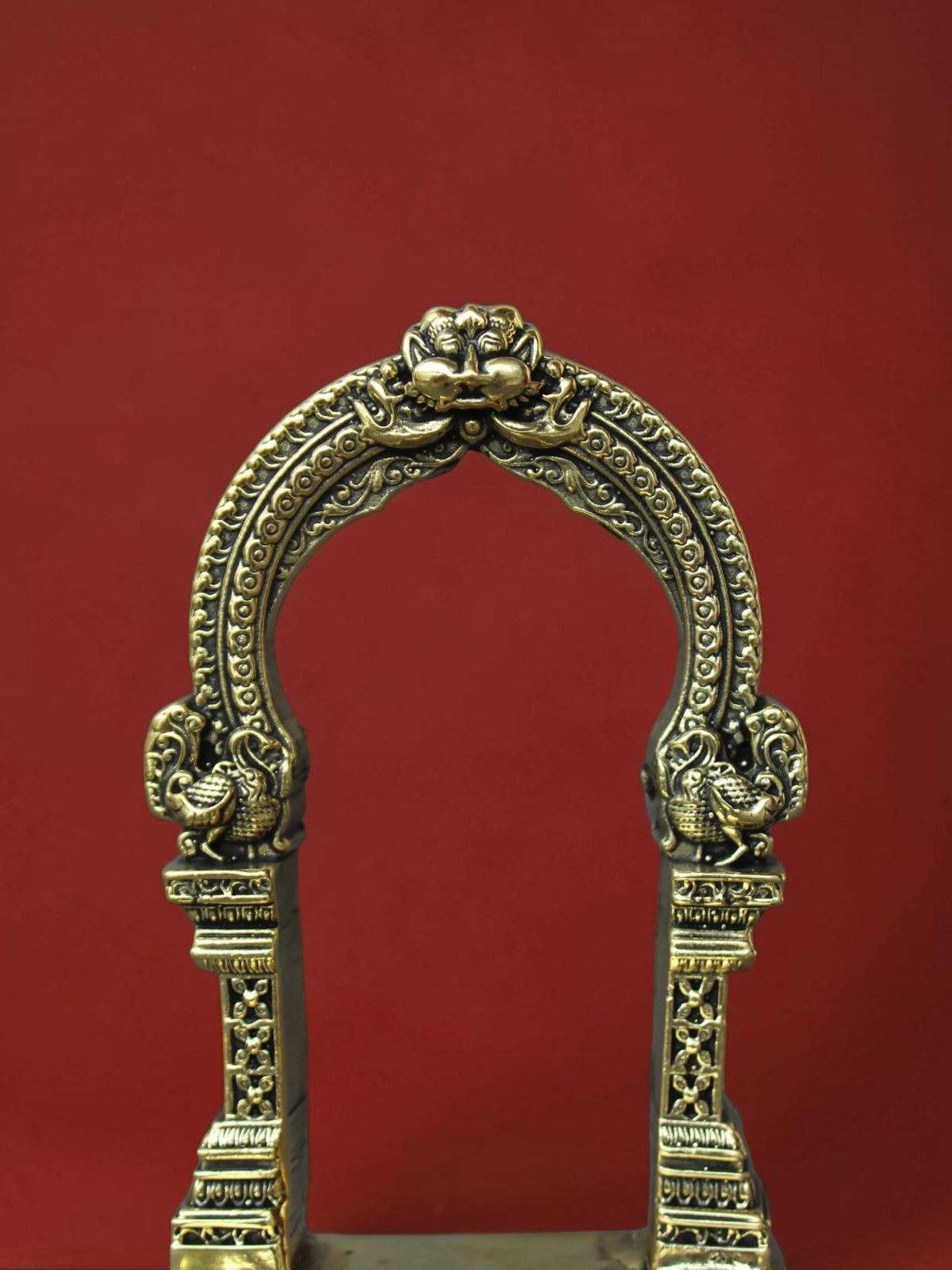 Rigvedaa™ handcrafted brass archway idol stand with intricate scrollwork and sculpted motifs in a polished gold finish.