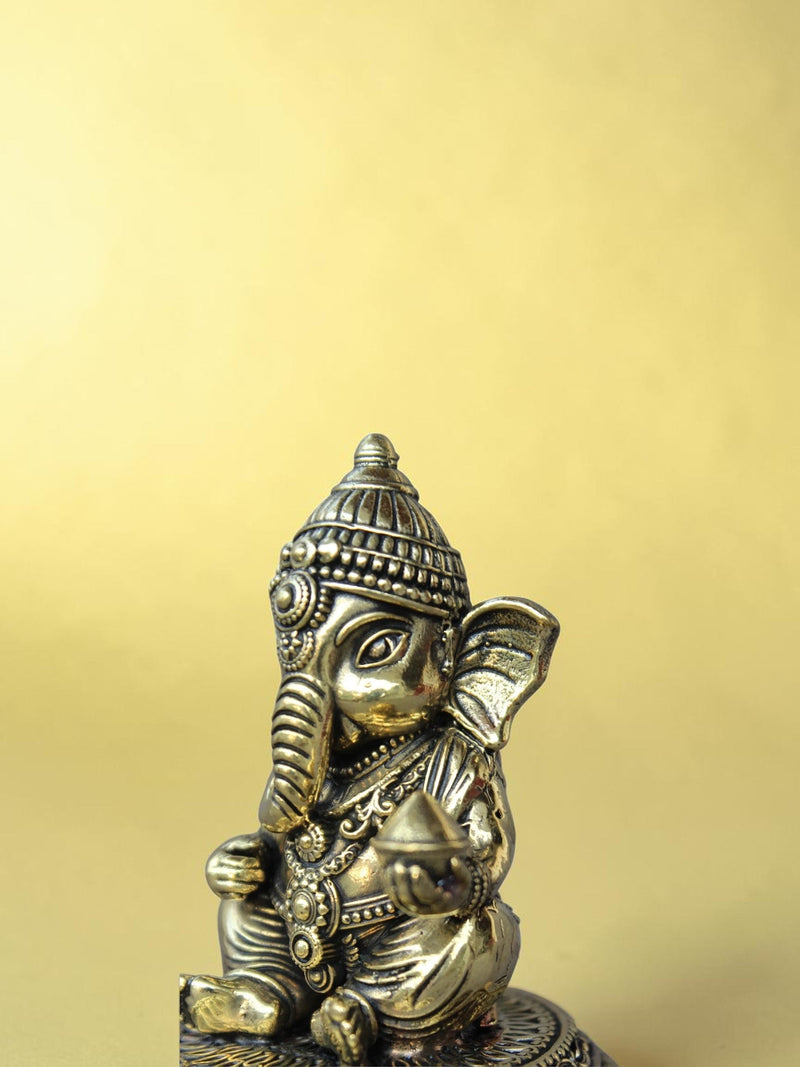 Rigvedaa™ handcrafted brass Bal Ganesha idol in a seated pose with antique gold finish and intricate relief details.