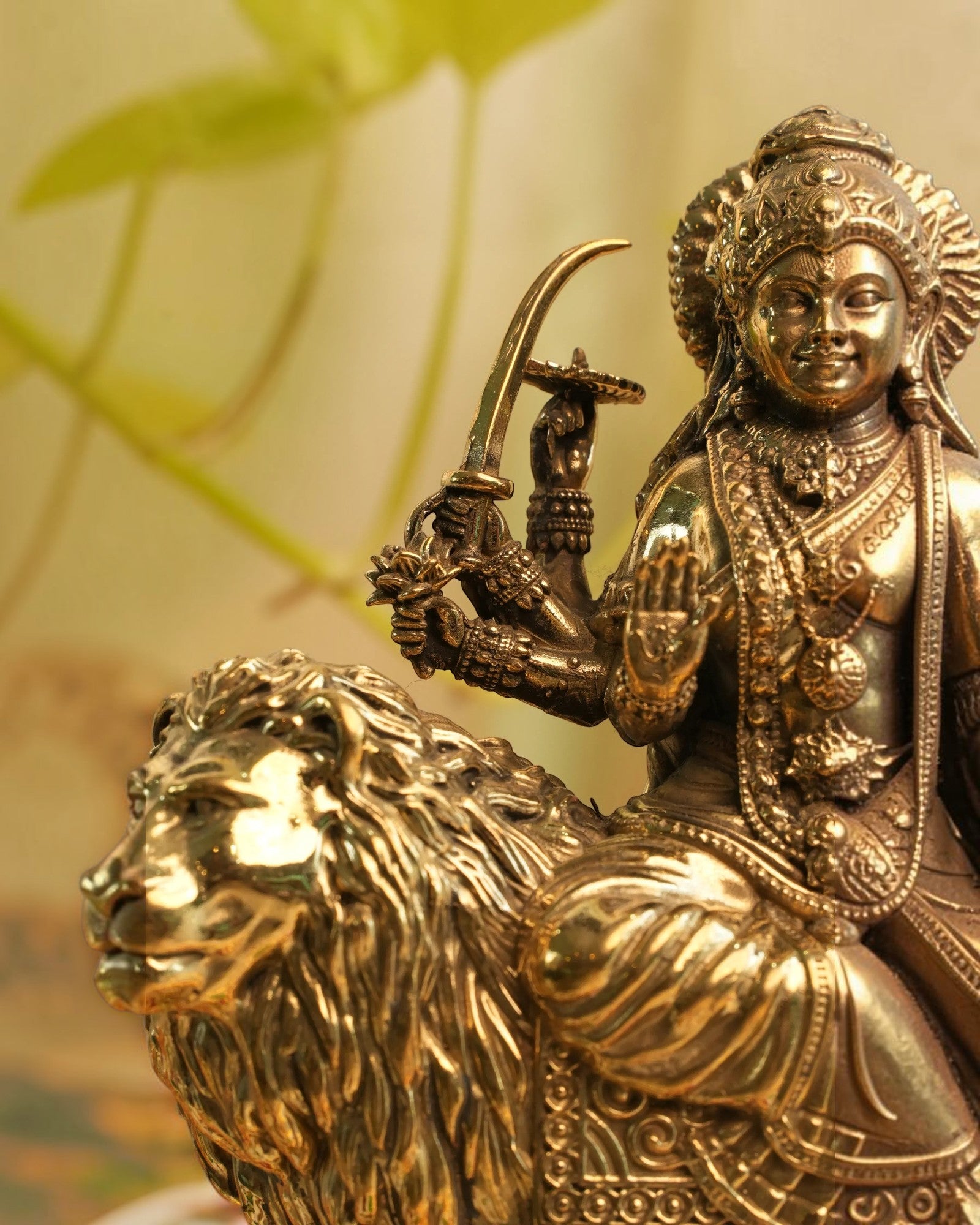 Rigvedaa™ brass Durga statue seated on a lion, holding weapons and in Abhaya Mudra. Golden patina finish.