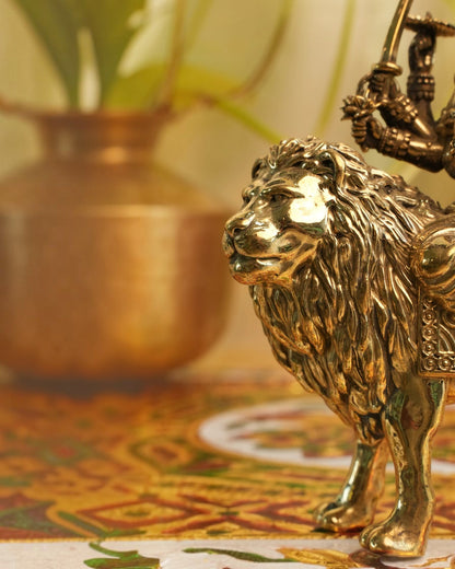 Rigvedaa brass Durga seated on lion murti, golden patina, intricate details, holding weapons, Abhaya Mudra.