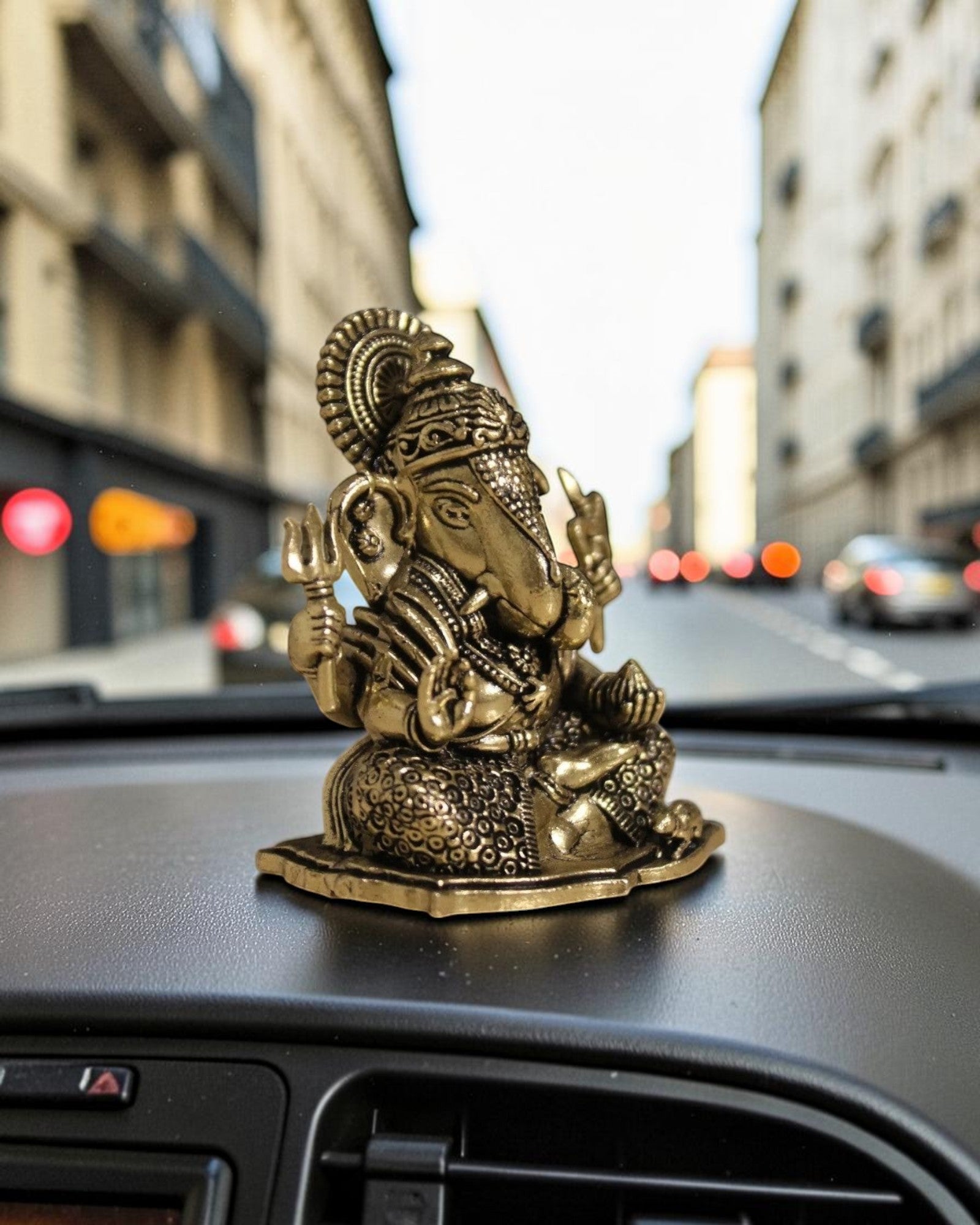 Rigvedaa™ brass Ganesha idol with intricate details, seated on a base, placed on a car dashboard.