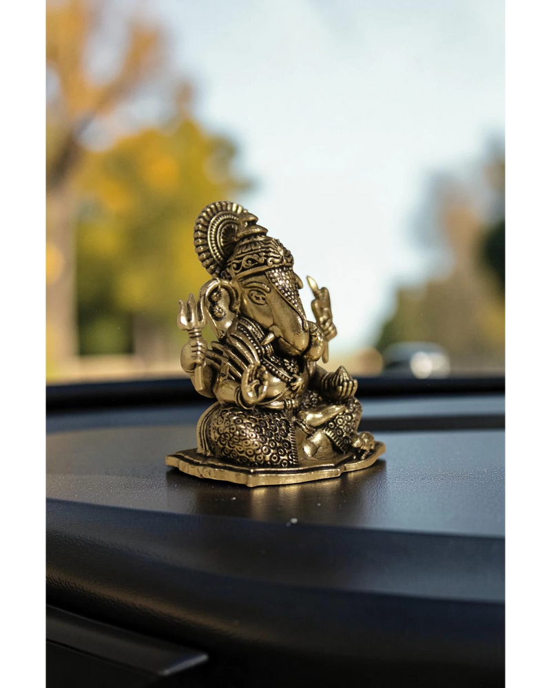 Rigvedaa™ brass Ganesha idol with intricate details, seated on a base, placed on a car dashboard.