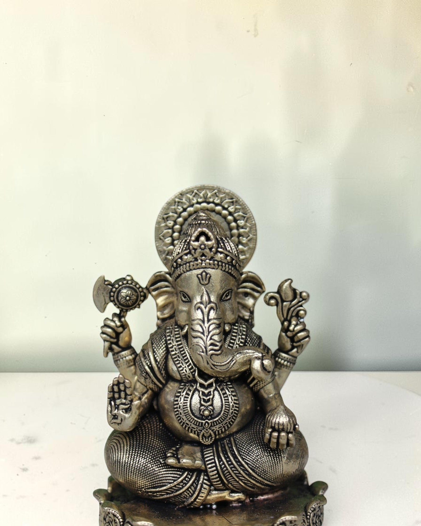 Rigvedaa™ antique brass Ganesha idol seated on a lotus base, holding an axe and a lotus flower.