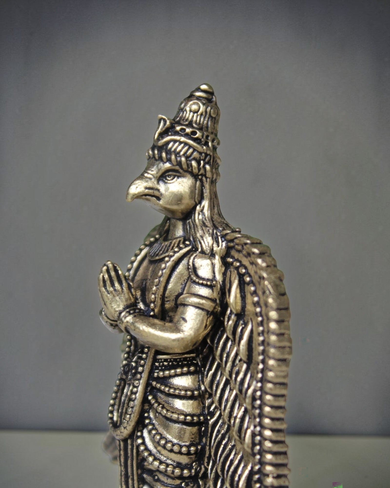 Rigvedaa brass Garuda statue with folded hands, detailed wings, and ornate headdress. Antique gold finish.