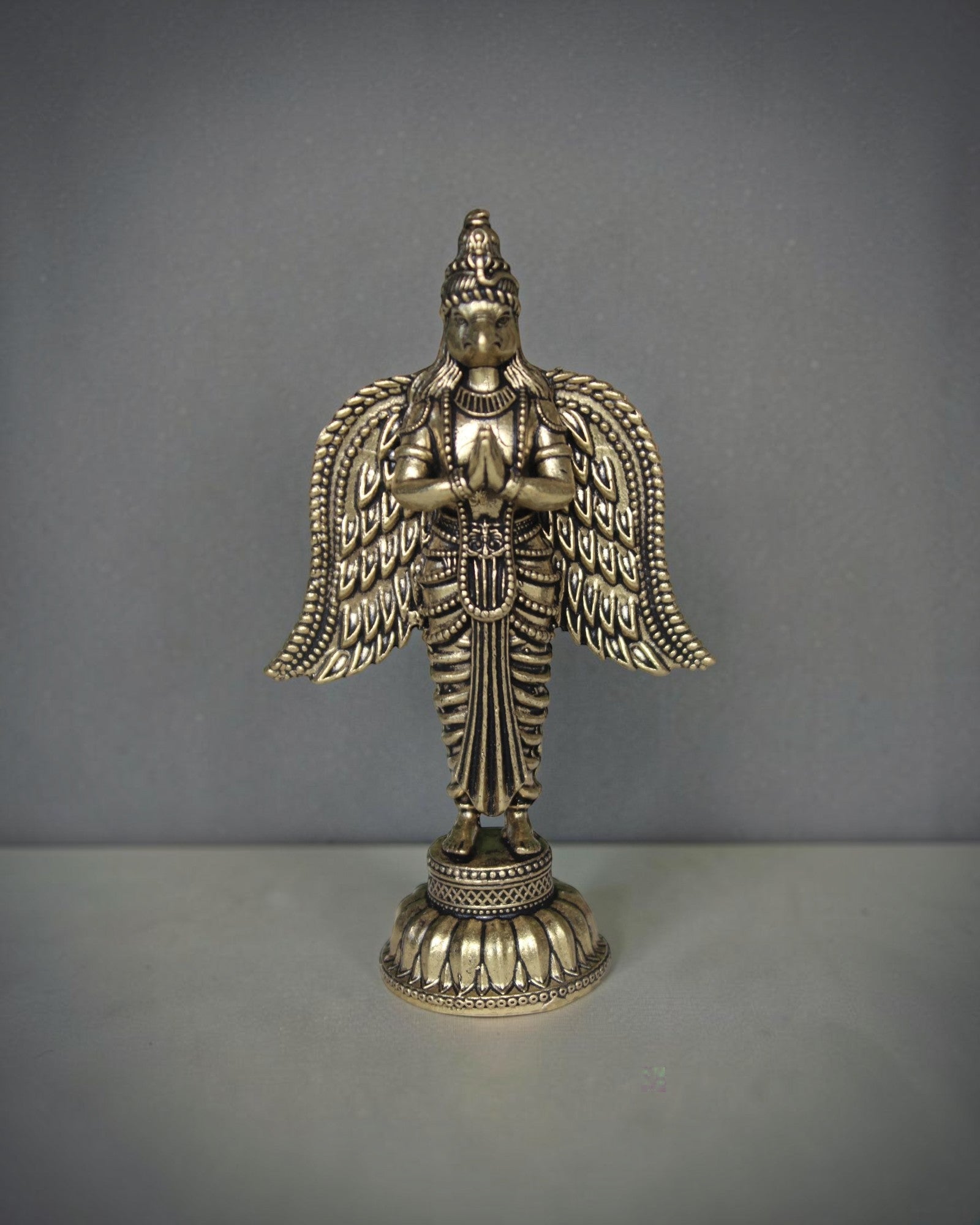 Rigvedaa brass Garuda statue with folded hands and spread wings, detailed antique gold finish, ideal for pooja decor.