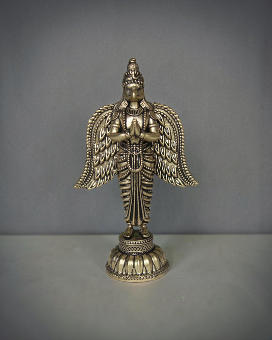 Rigvedaa brass Garuda statue with folded hands and spread wings, detailed antique gold finish, ideal for pooja decor.