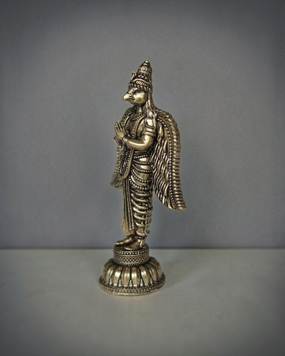 Rigvedaa brass Garuda statue with folded hands, detailed wings, and ornate base. Antique gold finish.