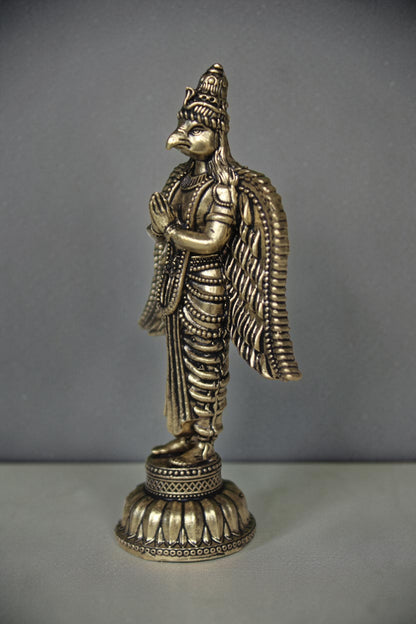 Rigvedaa brass Garuda statue with folded hands, detailed wings, and ornate base. Antique gold finish.