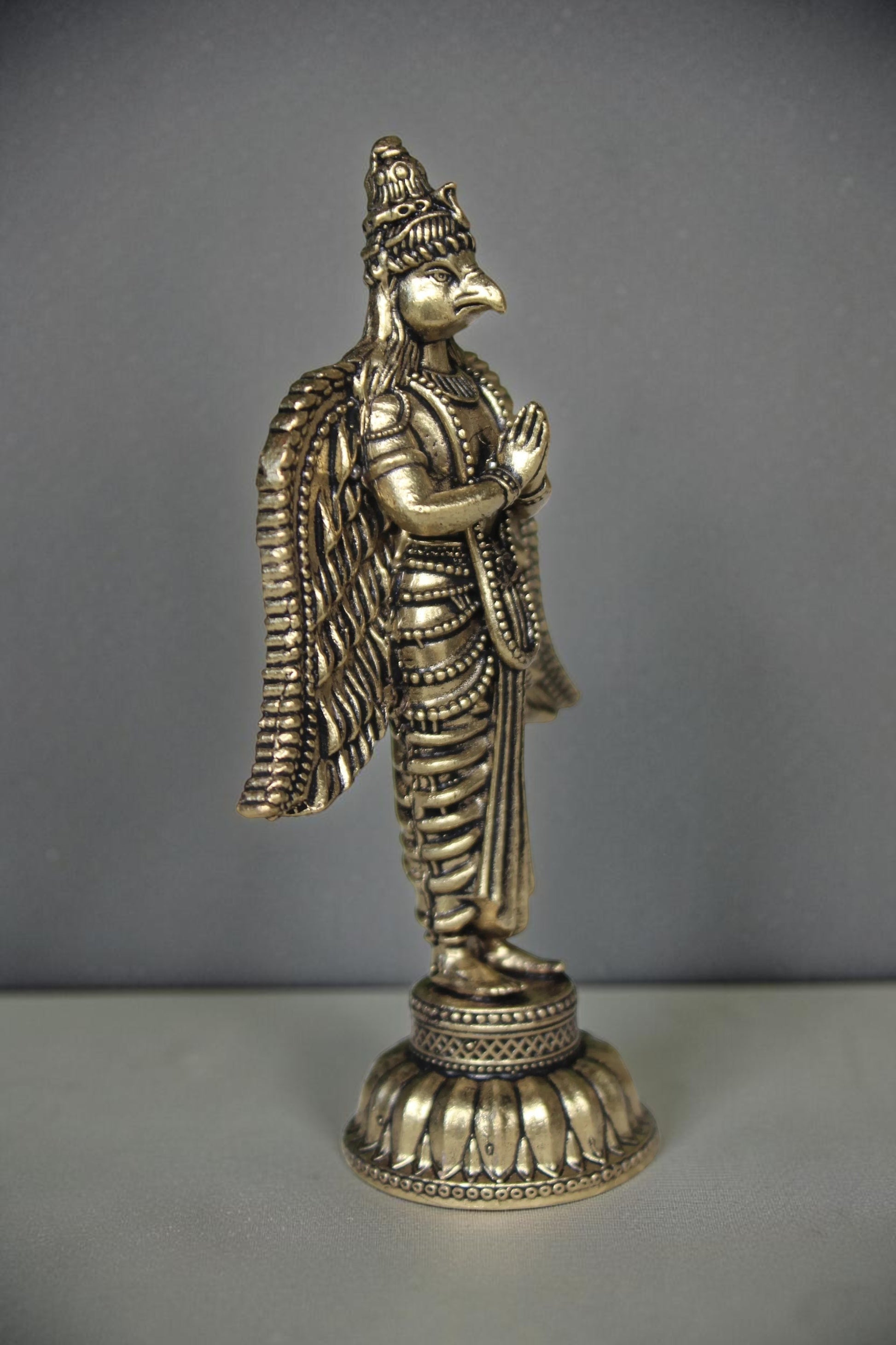 Rigvedaa brass Garuda statue with folded hands and spread wings, detailed antique gold finish, ideal for pooja decor.