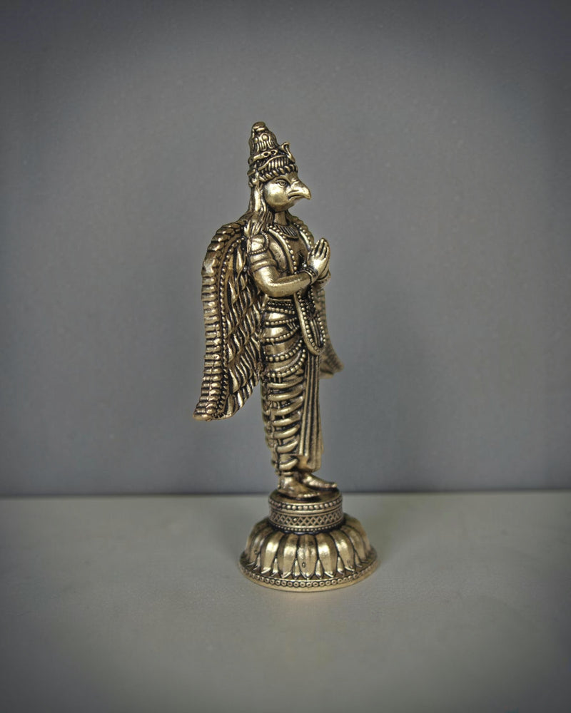Rigvedaa brass Garuda statue with folded hands and spread wings, detailed antique gold finish, ideal for pooja decor.