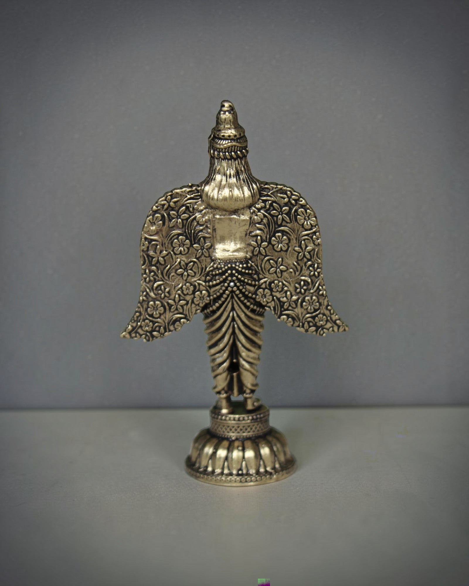 Rigvedaa brass Garuda statue with spread wings, intricate floral patterns, and antique gold finish. Ideal for pooja and home decor.