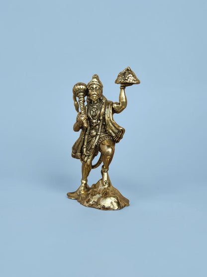 Rigvedaa™ brass Lord Hanuman idol holding a mace and mountain, featuring a polished golden finish on a blue background.