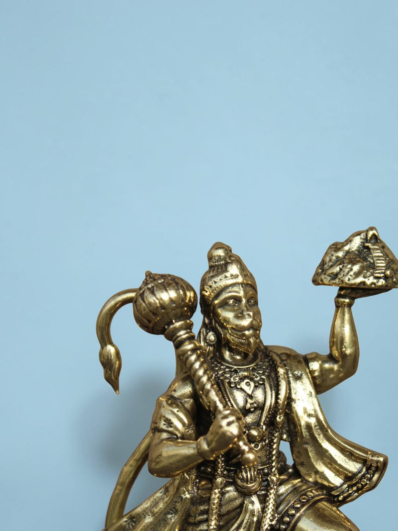 Rigvedaa™ brass Lord Hanuman idol holding a mace and mountain, featuring intricate golden details on a blue background.