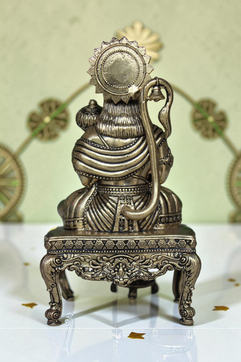 Rigvedaa™ brass Hanuman Ji idol sitting on an ornate throne, holding a mace. Golden finish, detailed craftsmanship.