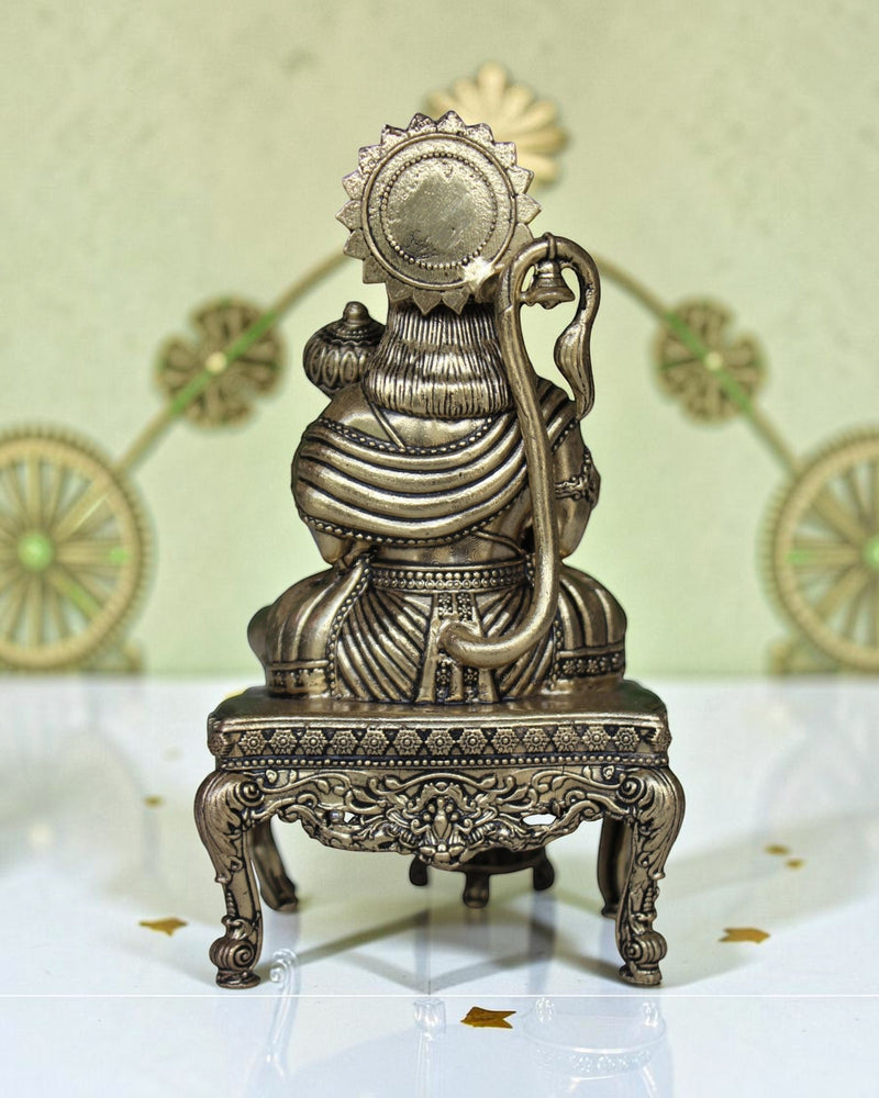 Rigvedaa™ brass Hanuman Ji idol sitting on an ornate throne, holding a mace. Golden finish, detailed craftsmanship.
