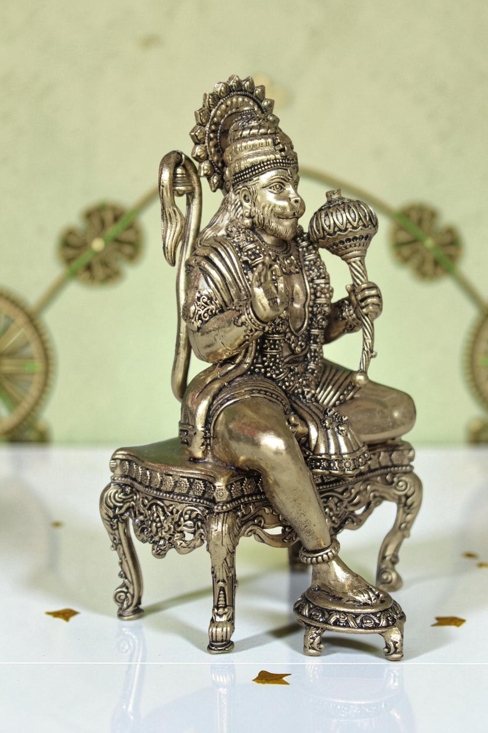 Rigvedaa™ brass Hanuman Ji idol sitting on an ornate throne, holding a mace. Golden finish, detailed craftsmanship.