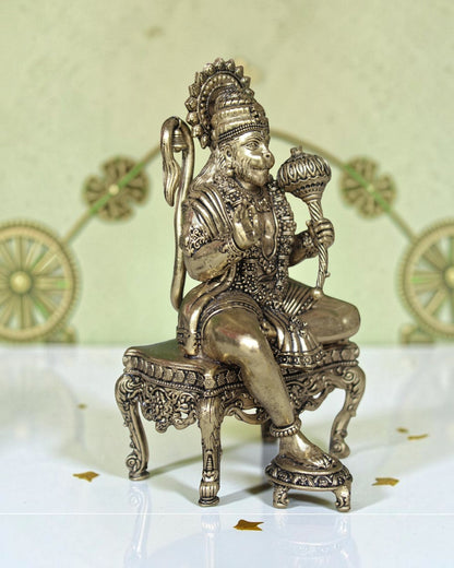 Rigvedaa™ brass Hanuman Ji idol sitting on an ornate throne, holding a mace. Golden finish, detailed craftsmanship.