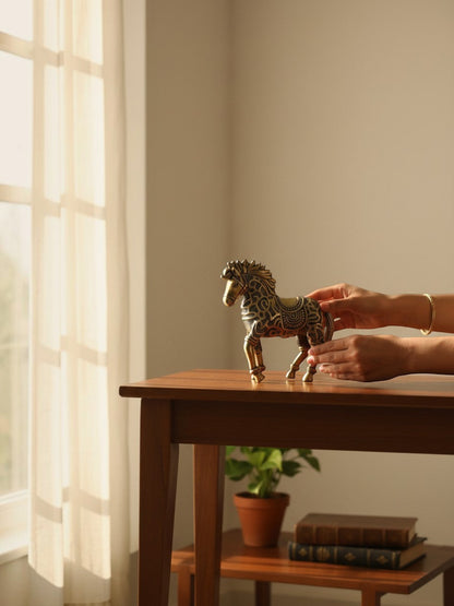 Rigvedaa™ decorative brass horse statue with intricate relief patterns, held on a wooden table near a sunlit window.
