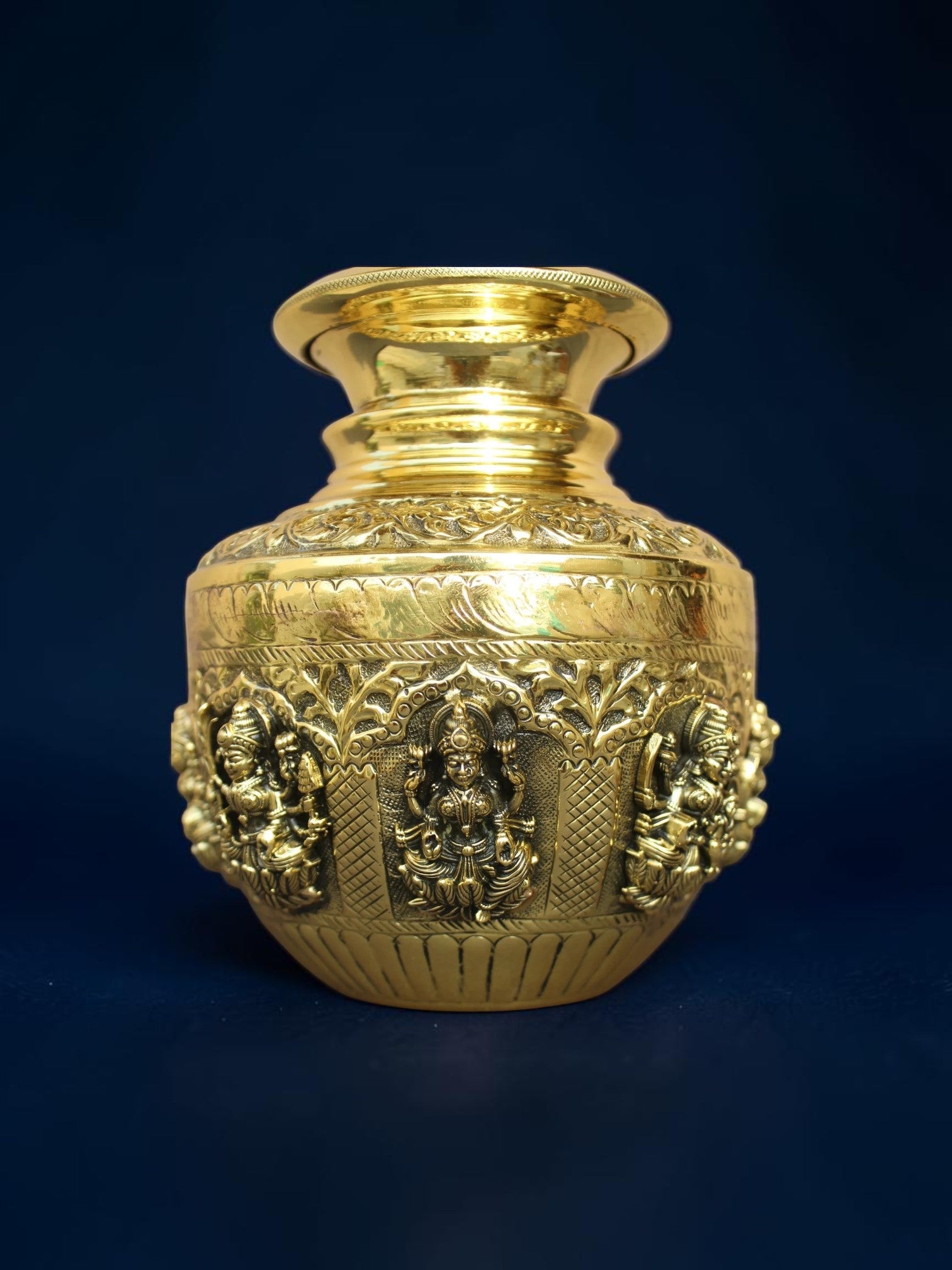Rigvedaa™ handcrafted brass kalash pot with intricate embossed deity carvings and a polished gold-tone finish.