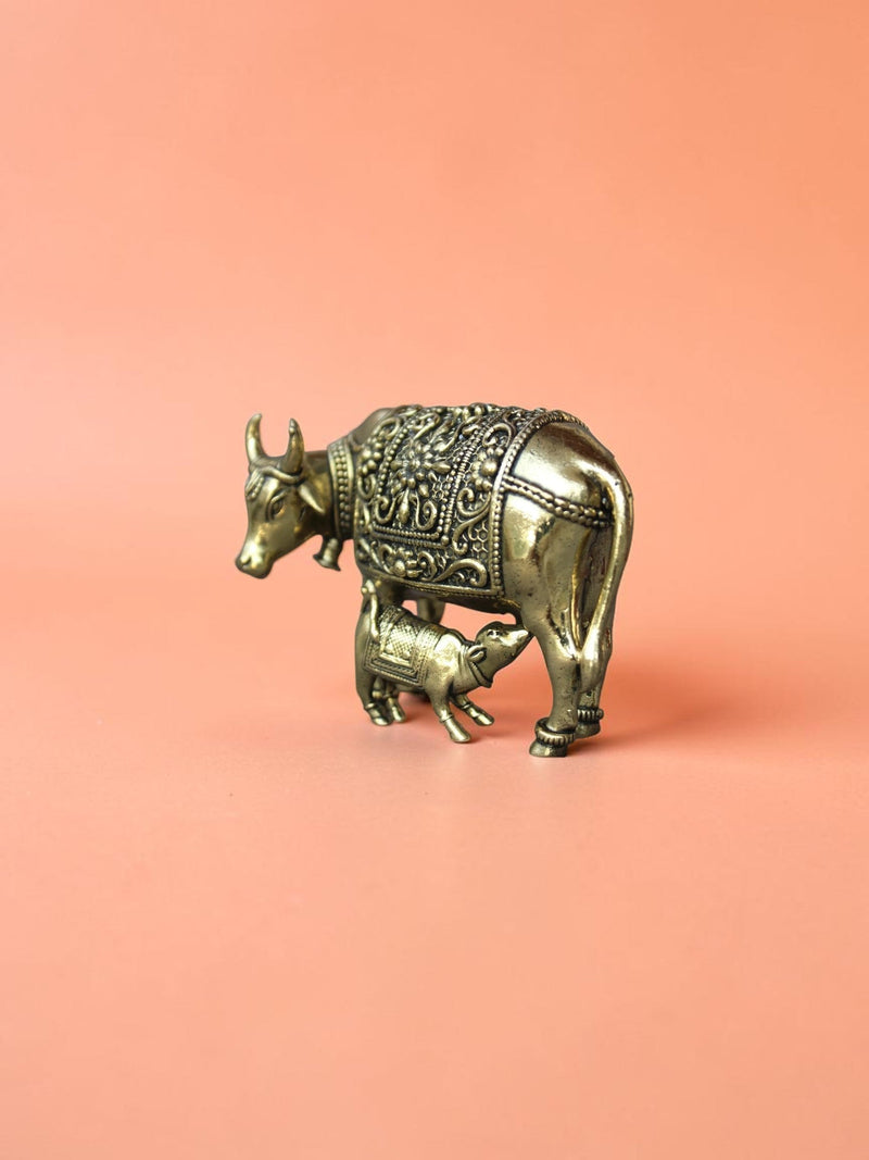 Rigvedaa™ brass Kamdhenu cow and calf idol featuring intricate floral carvings and a polished golden finish.