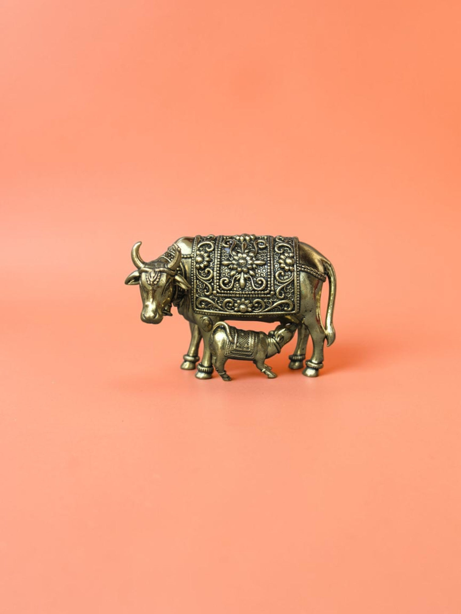 Rigvedaa™ brass Kamdhenu cow and calf idol featuring intricate floral carvings and a polished golden finish.