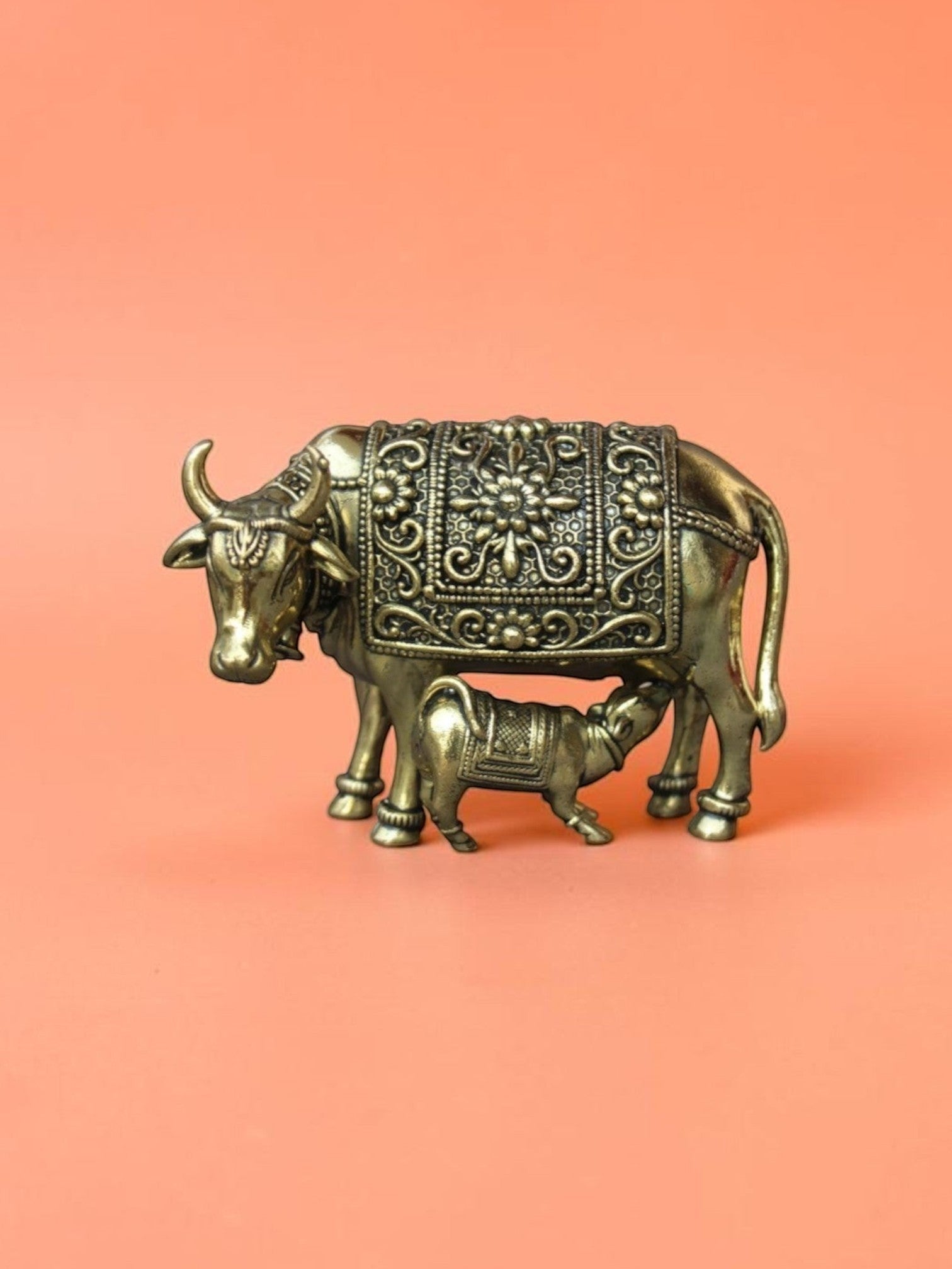 Rigvedaa™ brass Kamdhenu cow and calf idol featuring intricate hand-etched floral carvings and a polished golden finish.