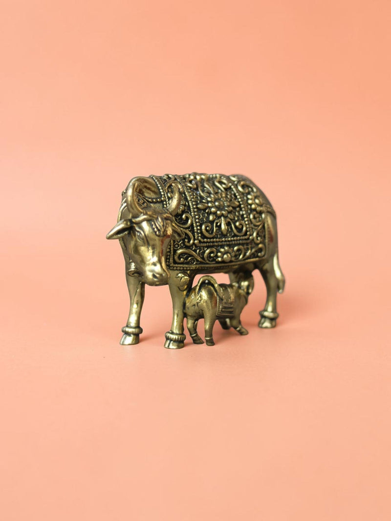Rigvedaa™ brass Kamdhenu cow and calf idol featuring intricate hand-etched floral carvings and a polished gold finish.