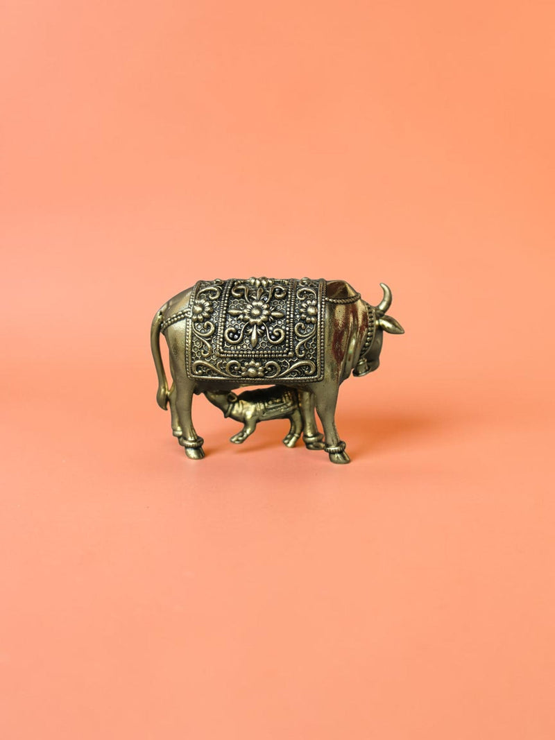Rigvedaa™ brass Kamdhenu cow and calf idol featuring intricate hand-etched floral carvings and a polished golden finish.