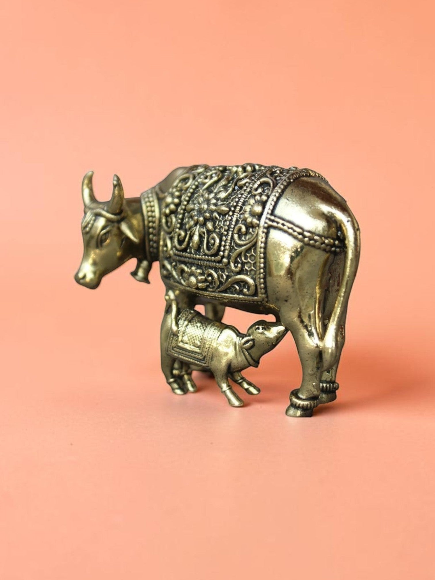 Rigvedaa™ brass Kamdhenu cow and calf idol featuring intricate hand-etched floral carvings and a golden finish.