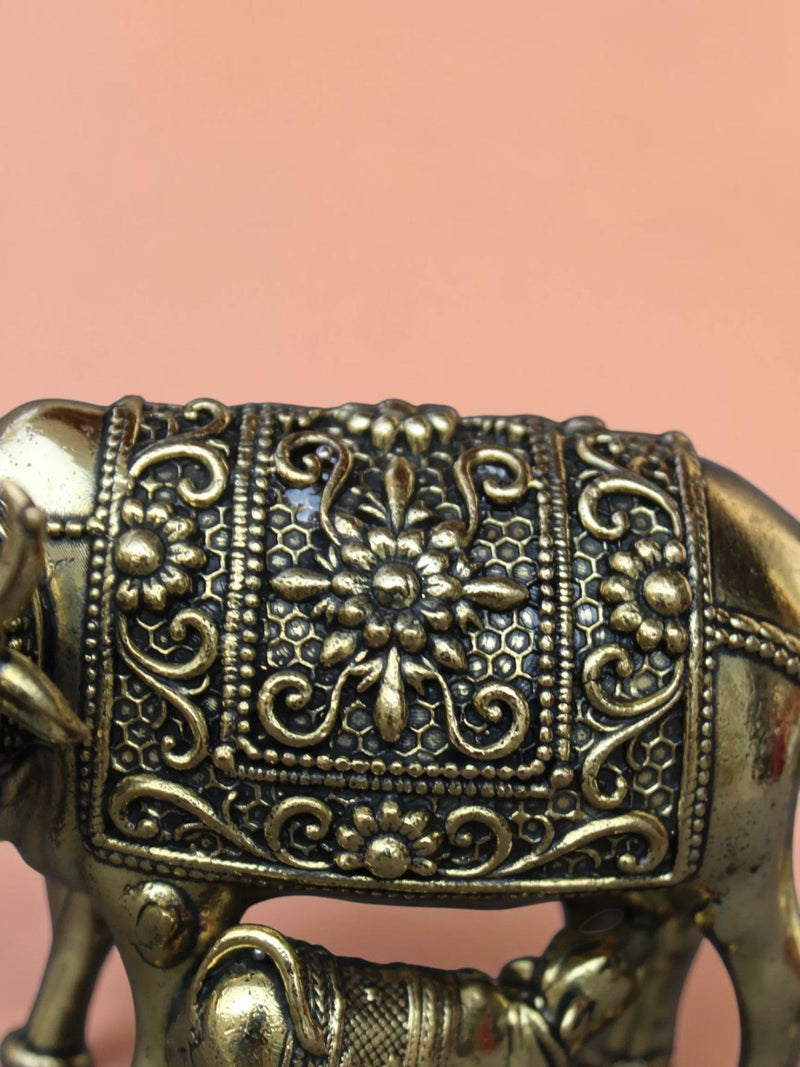 Close-up of Rigvedaa™ brass Kamdhenu cow and calf idol featuring intricate hand-etched floral relief and golden finish.