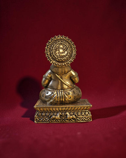 Rigvedaa™ brass Kuber idol sitting on a decorative chowki, holding a money pot. Golden patina finish.