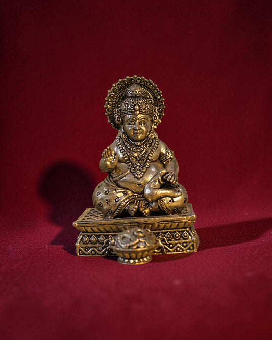 Rigvedaa™ brass Kuber idol sitting on a chowki, holding a money pot and mongoose. Golden patina finish.