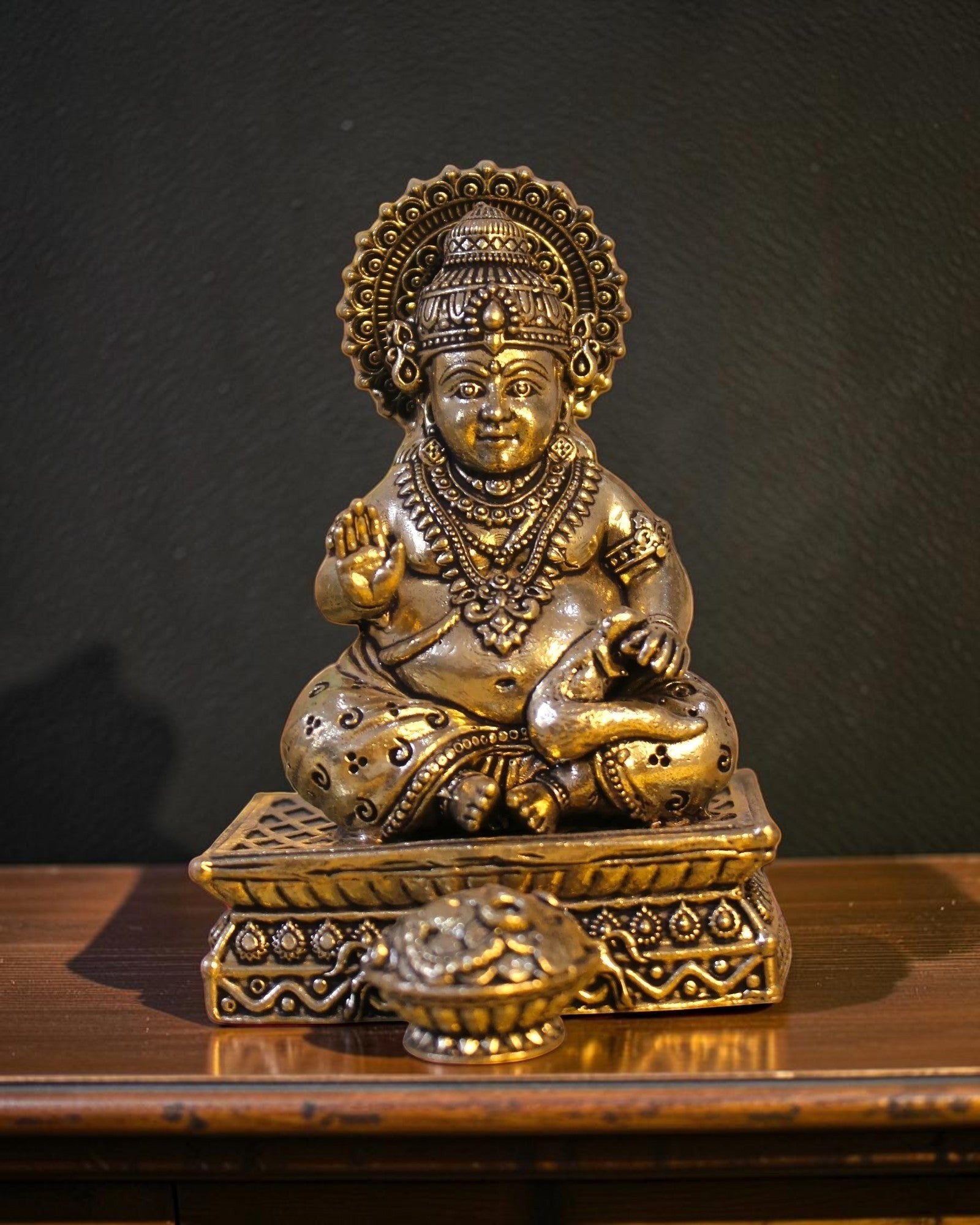 Rigvedaa™ brass Kuber idol seated on a decorative chowki, holding a pot of coins. Intricately detailed with crown and jewelry.