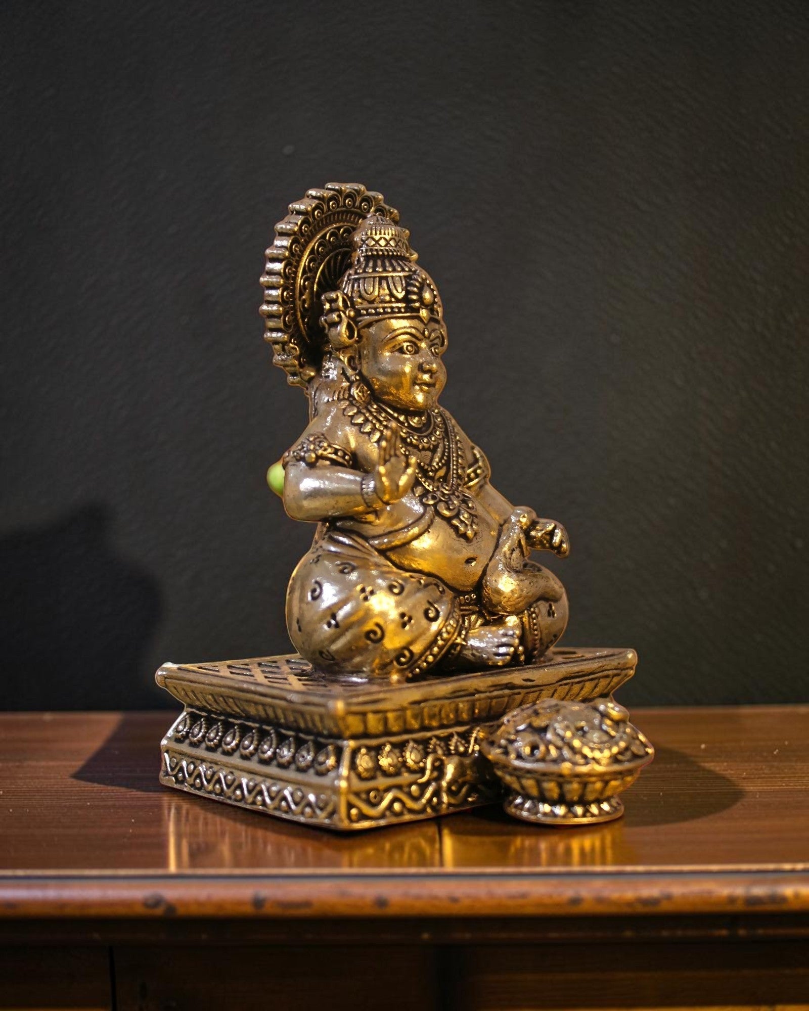 Rigvedaa™ brass Kuber idol seated on a decorative chowki, holding a pot of coins. Detailed with ornate crown and jewelry.