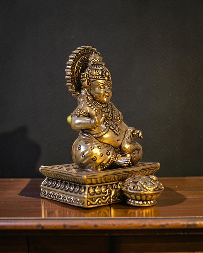 Rigvedaa™ brass Kuber idol seated on a decorative chowki, holding a pot of coins. Detailed with ornate crown and jewelry.