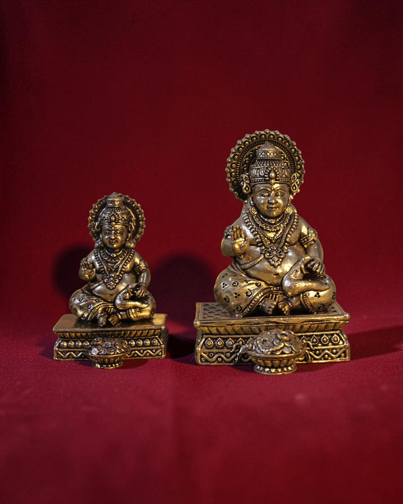 Rigvedaa™ Brass Kuber idol sitting on a chowki, holding a money pot and mongoose. Golden patina finish.