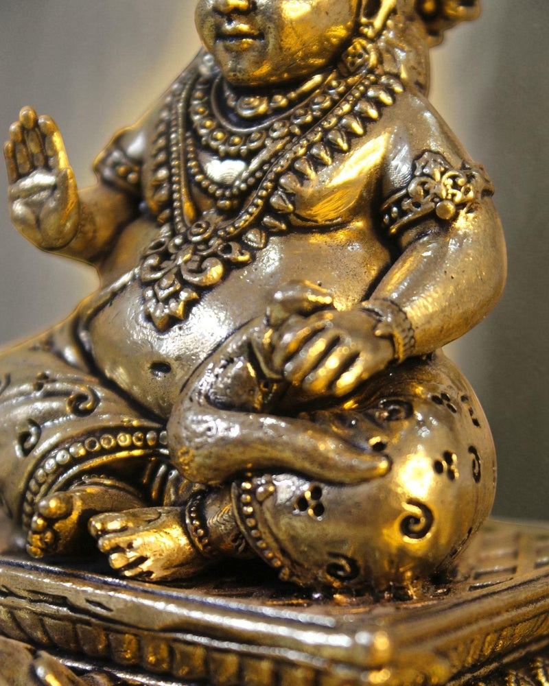 Rigvedaa™ antique brass Kuber idol seated on a decorative chowki, holding a pot of coins. Detailed ornamentation and crown.