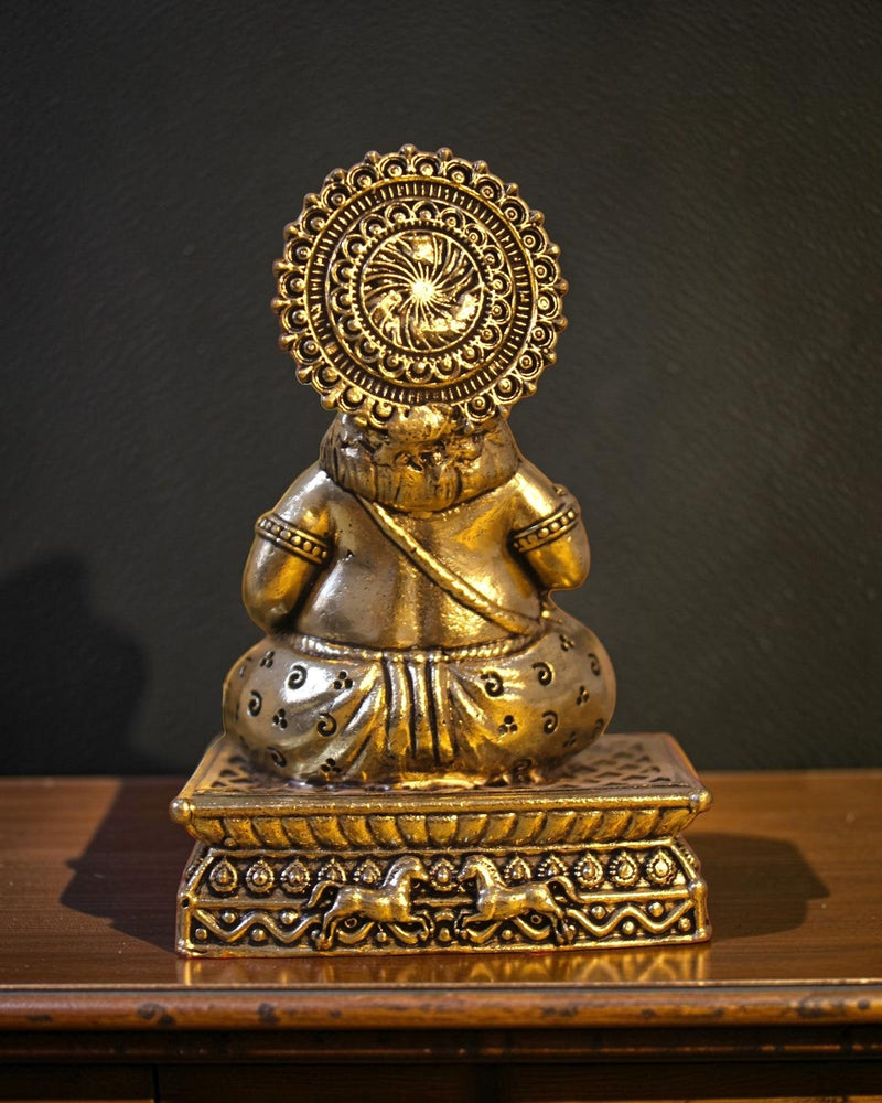 Rigvedaa brass Kuber idol sitting on a decorative chowki pedestal, adorned with ornate crown and jewelry, symbolizing wealth and prosperity.