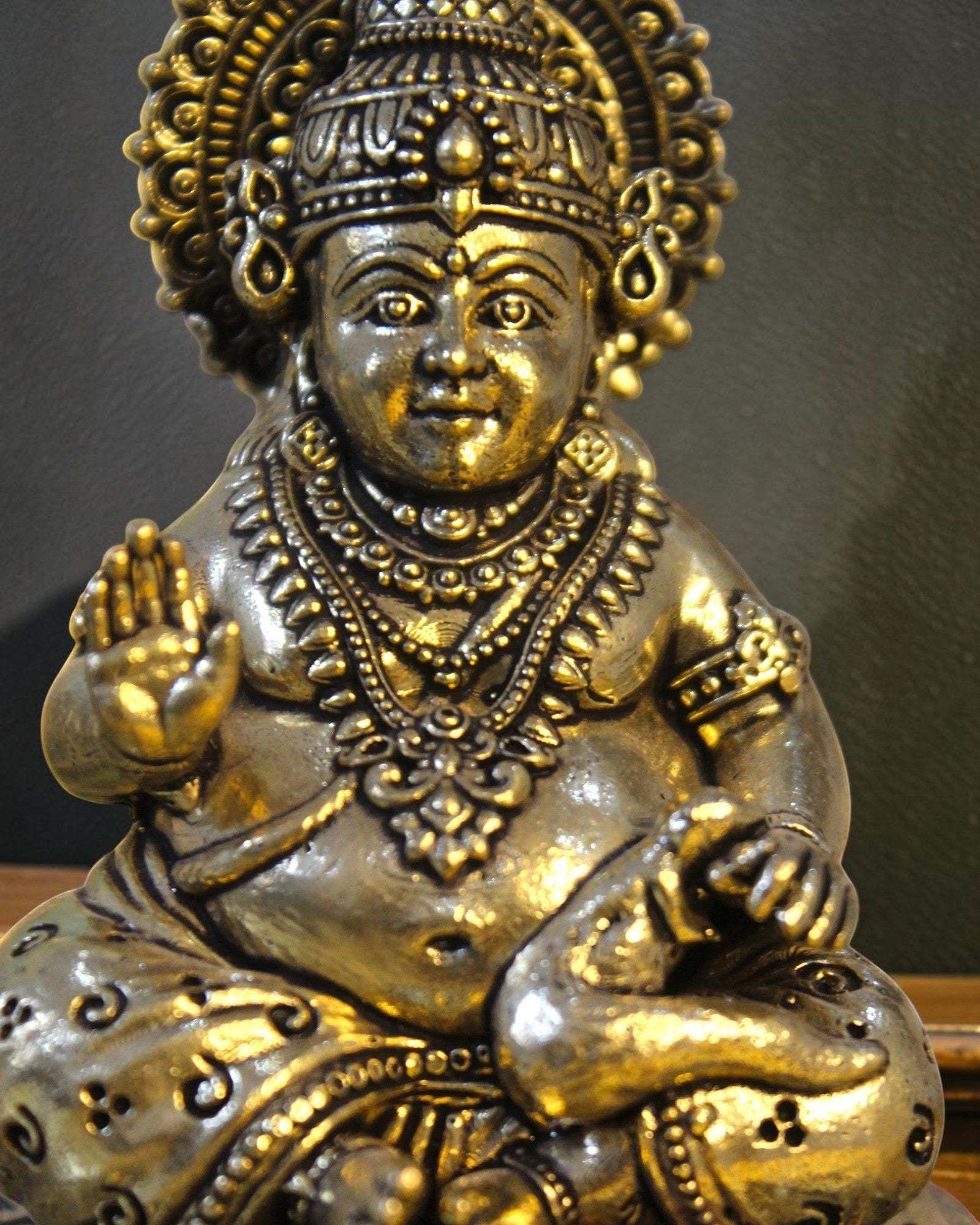 Rigvedaa brass Kuber idol sitting on a decorative chowki, adorned with ornate crown, jewelry, and coin pot. Symbolizes wealth and prosperity.