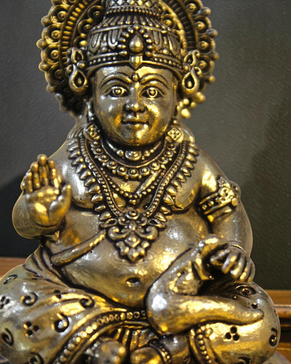 Rigvedaa brass Kuber idol sitting on a decorative chowki, adorned with ornate crown, jewelry, and coin pot. Symbolizes wealth and prosperity.