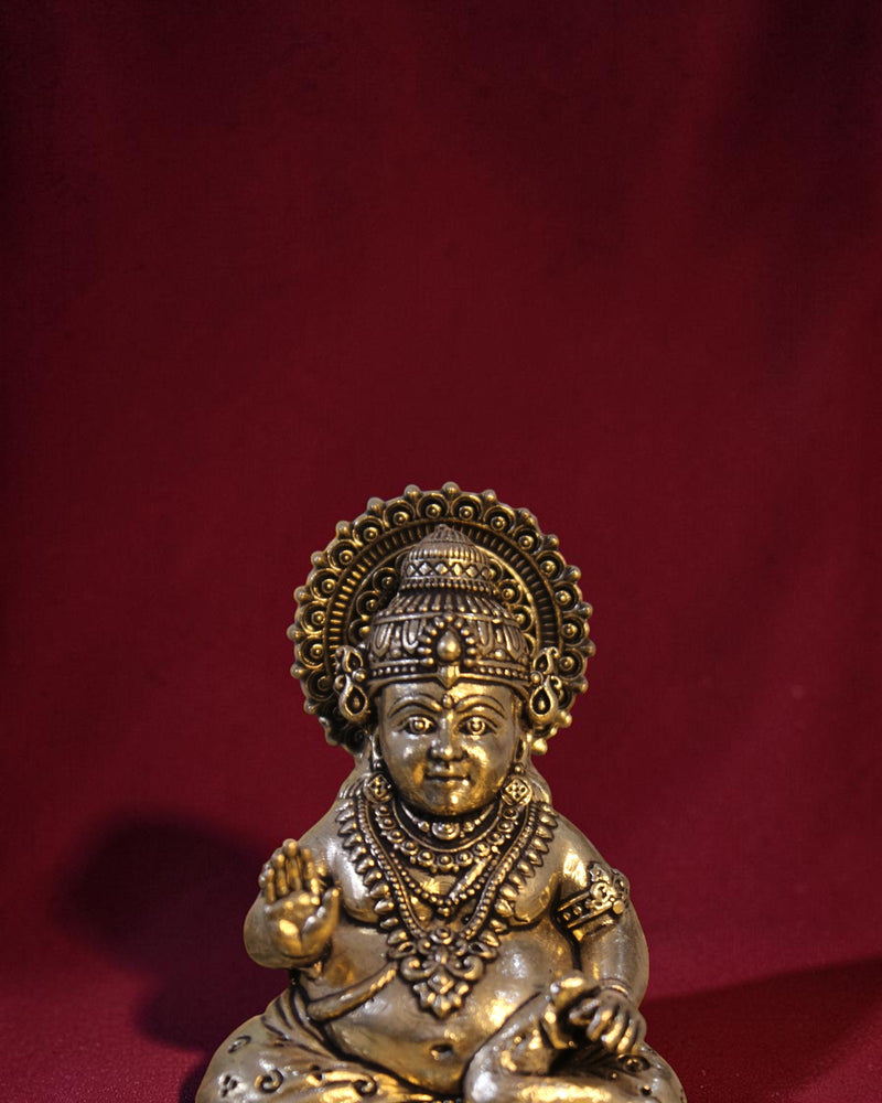 Rigvedaa™ Brass Kuber idol sitting on a chowki, holding a money pot and mongoose. Golden patina finish.