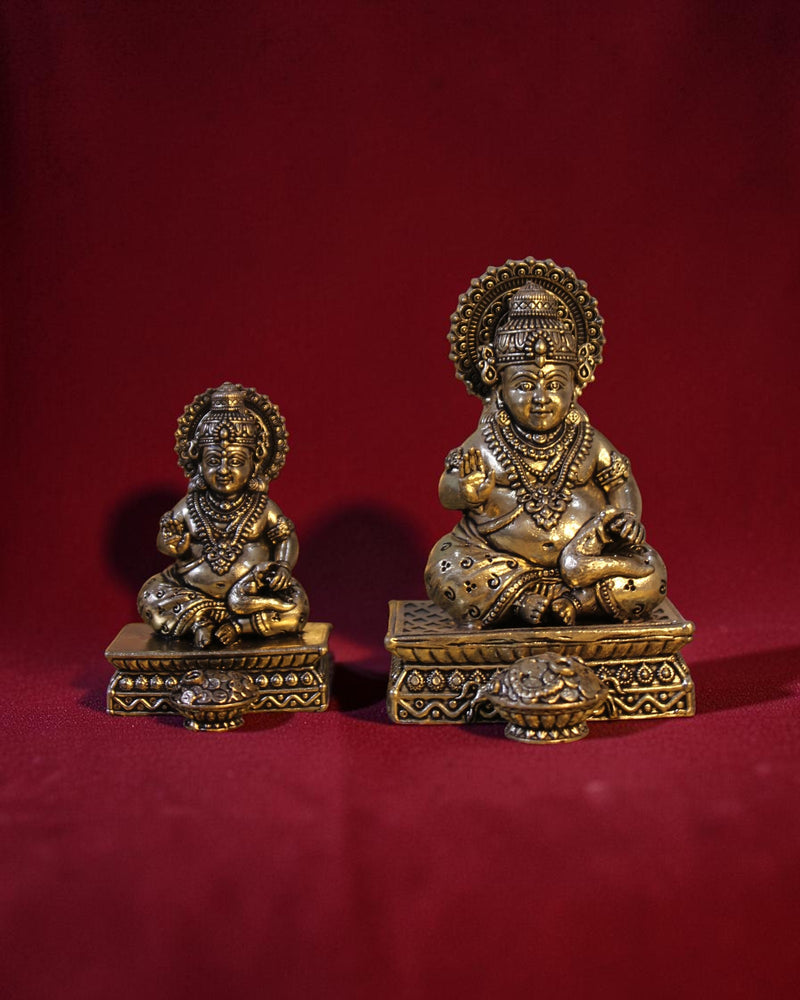 Rigvedaa™ brass Kuber idol sitting on a chowki, holding a money pot and mongoose. Detailed ornamentation, golden patina.